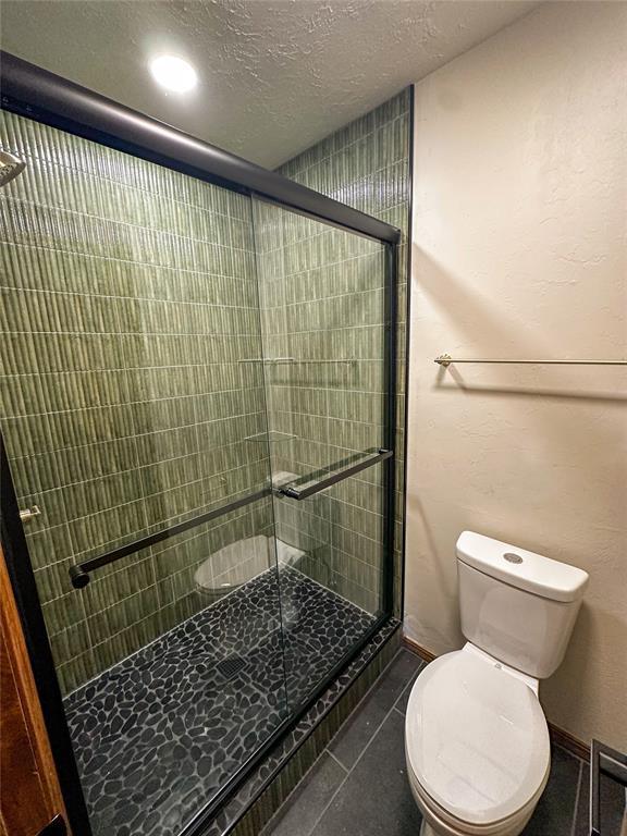 full bathroom featuring a stall shower, baseboards, toilet, tile patterned floors, and a textured ceiling