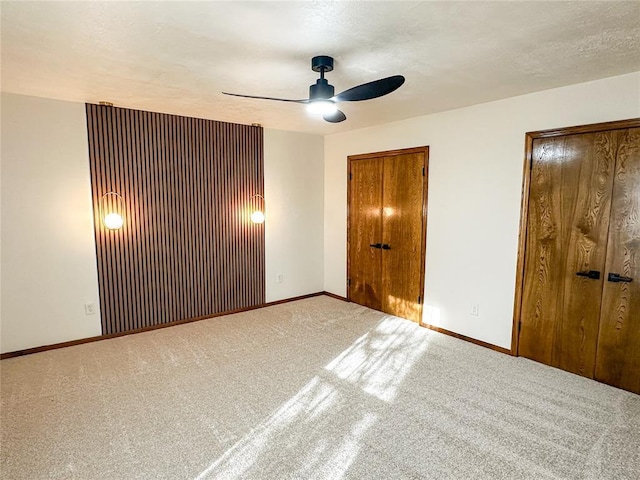 unfurnished bedroom with baseboards, a ceiling fan, a textured ceiling, carpet flooring, and two closets