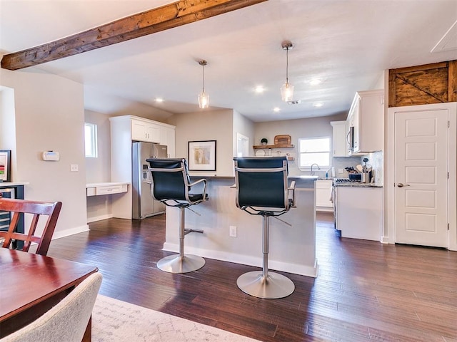 kitchen featuring a breakfast bar, beam ceiling, stainless steel appliances, dark wood-type flooring, and white cabinetry