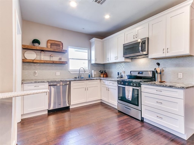 kitchen with light stone countertops, dark wood finished floors, a sink, white cabinets, and appliances with stainless steel finishes