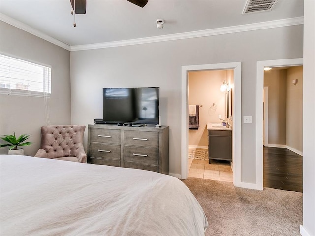 carpeted bedroom with visible vents, ornamental molding, ensuite bathroom, a sink, and baseboards