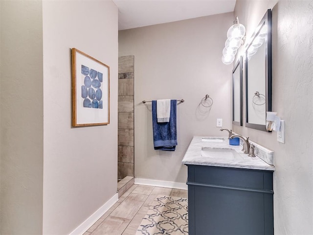 bathroom with double vanity, baseboards, tiled shower, and a sink