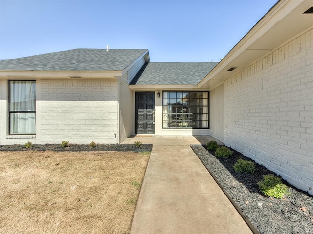 entrance to property with roof with shingles and brick siding