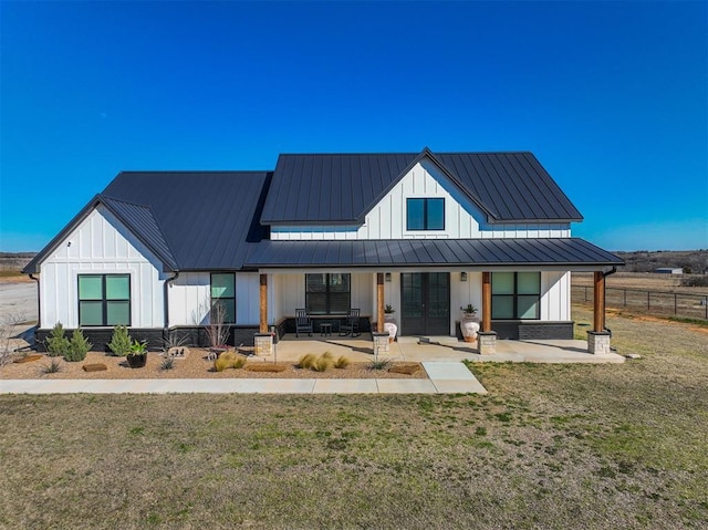 modern farmhouse style home featuring a front yard, fence, a standing seam roof, board and batten siding, and metal roof