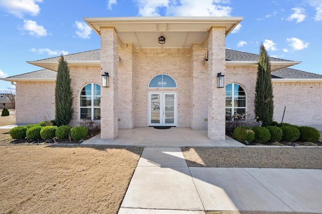 view of exterior entry with a shingled roof, french doors, and brick siding