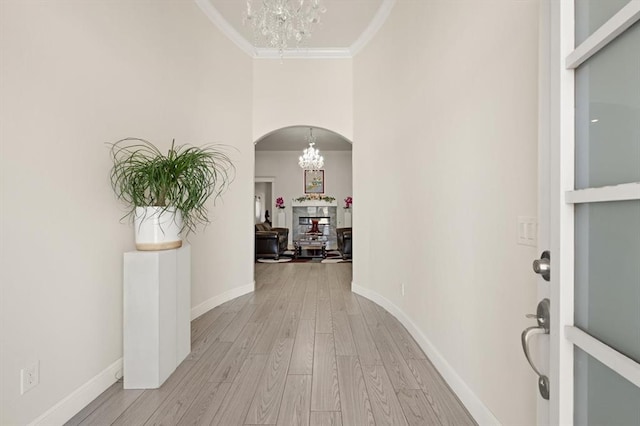 foyer entrance featuring a chandelier, light wood-type flooring, crown molding, and arched walkways