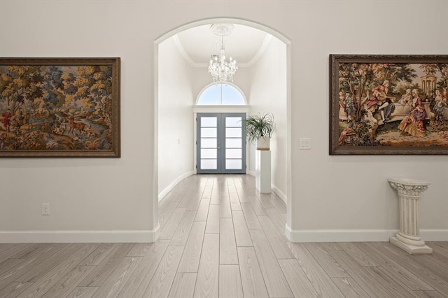 foyer entrance featuring wood finished floors, baseboards, ornamental molding, french doors, and an inviting chandelier