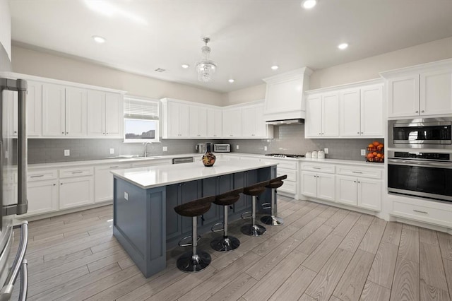 kitchen with a breakfast bar area, white cabinetry, appliances with stainless steel finishes, backsplash, and light wood finished floors