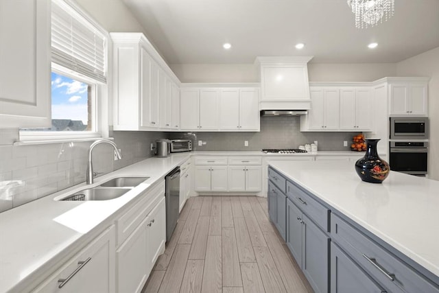 kitchen with white cabinets, light wood-style flooring, gray cabinets, stainless steel appliances, and a sink