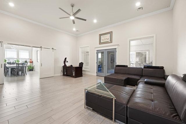 living room featuring light wood-type flooring, a barn door, visible vents, and crown molding