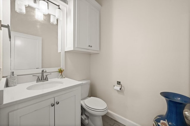 half bath featuring baseboards, vanity, toilet, and wood finished floors