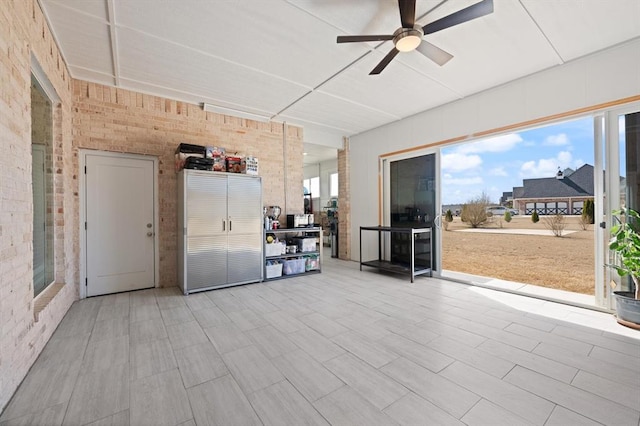 interior space with a ceiling fan and brick wall