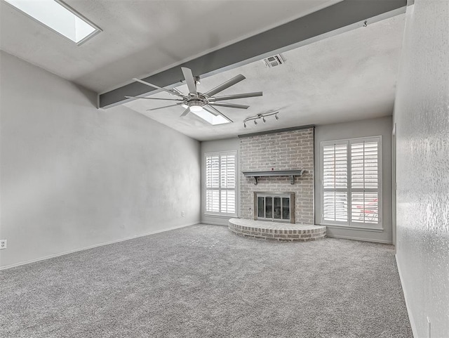 unfurnished living room with carpet, a skylight, visible vents, a ceiling fan, and a brick fireplace