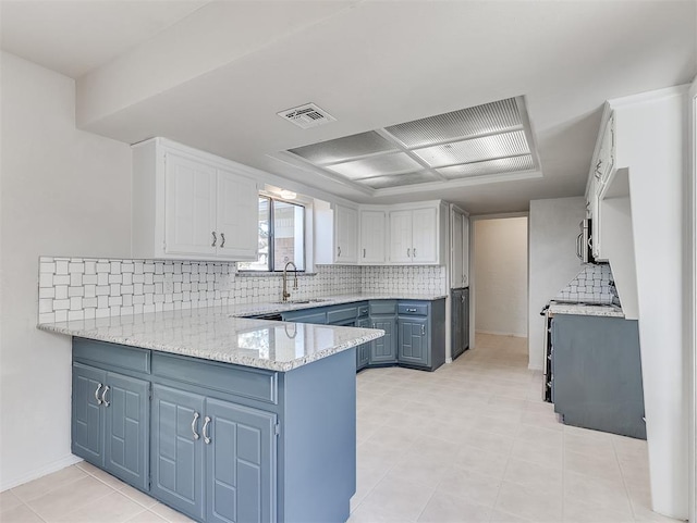 kitchen with tasteful backsplash, visible vents, a sink, blue cabinets, and a peninsula