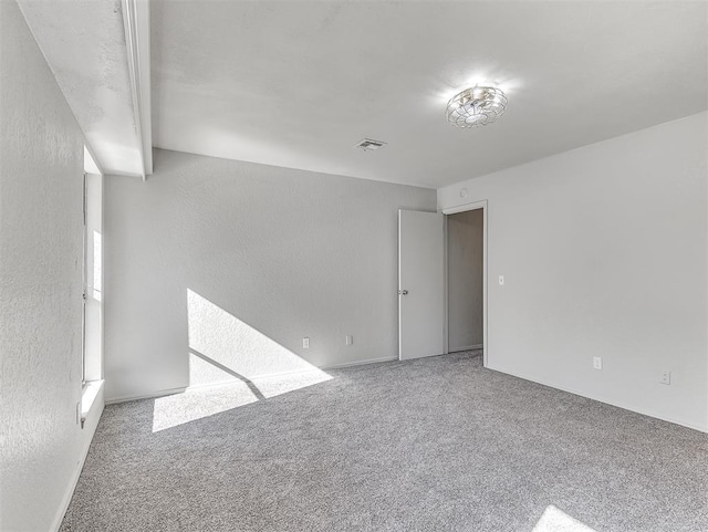 spare room with carpet floors, visible vents, and a textured wall