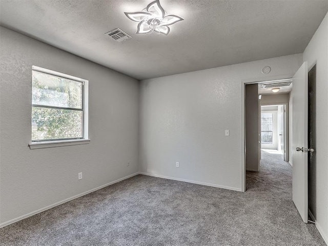 empty room featuring carpet floors, visible vents, a textured ceiling, and a textured wall