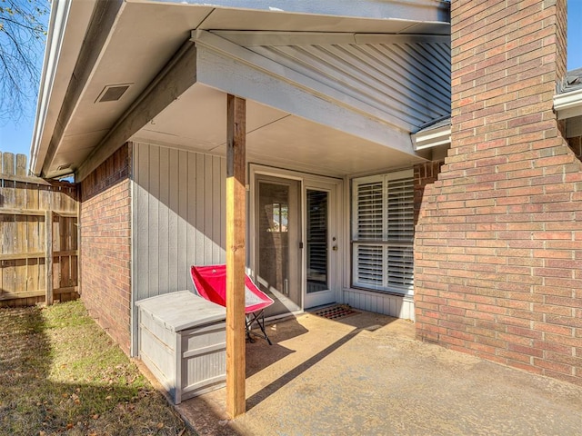 entrance to property featuring a patio area, visible vents, fence, and brick siding