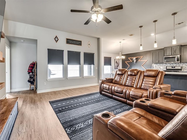 living room with light wood-type flooring, visible vents, baseboards, and ceiling fan with notable chandelier