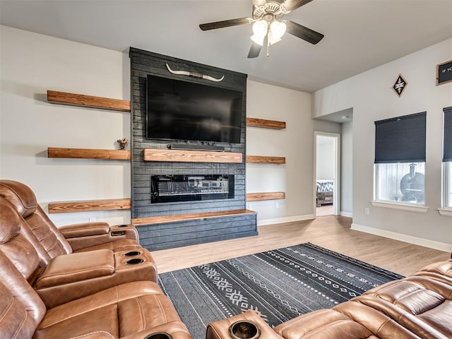 living area featuring a ceiling fan, a fireplace, baseboards, and wood finished floors