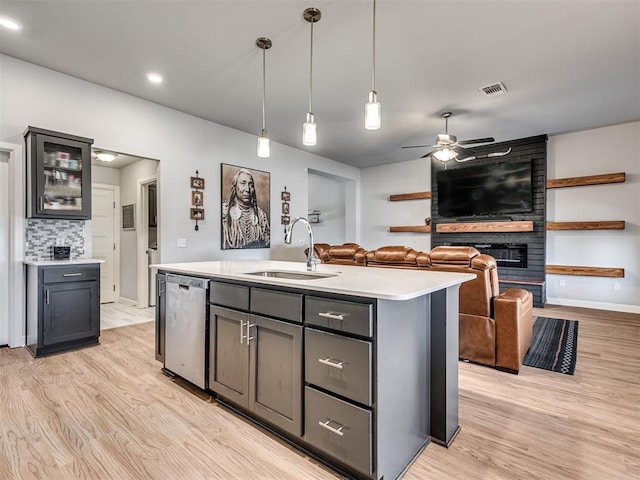 kitchen with light countertops, stainless steel dishwasher, light wood-style floors, a large fireplace, and a sink