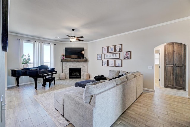 living room with arched walkways, a fireplace, light wood-style flooring, a ceiling fan, and ornamental molding