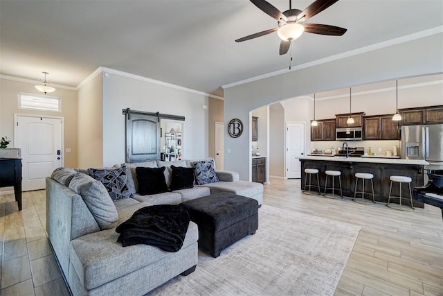 living room with light wood finished floors, a barn door, arched walkways, a ceiling fan, and ornamental molding