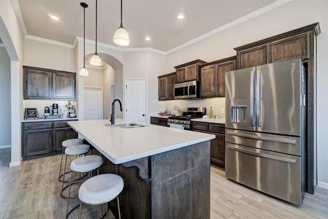 kitchen featuring arched walkways, a sink, dark brown cabinets, appliances with stainless steel finishes, and a center island with sink