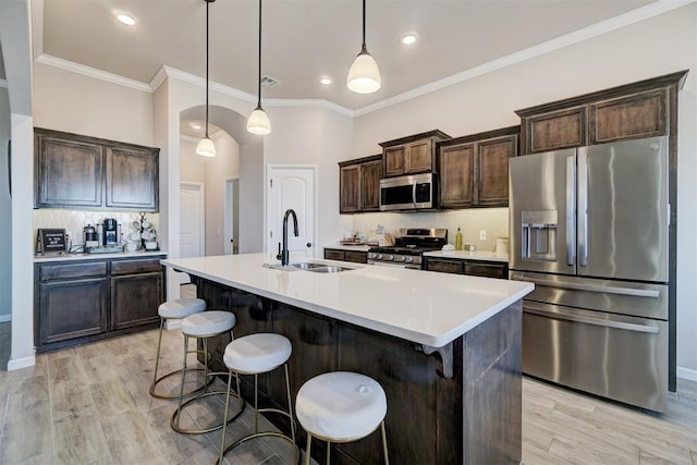 kitchen with decorative backsplash, appliances with stainless steel finishes, dark brown cabinets, a kitchen bar, and a sink