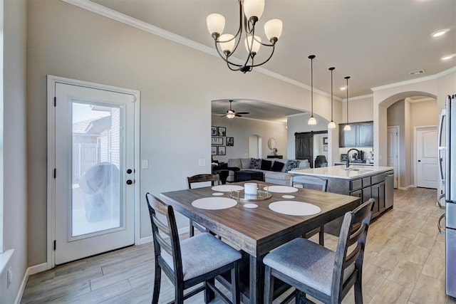 dining area with arched walkways, ceiling fan with notable chandelier, baseboards, ornamental molding, and light wood-type flooring