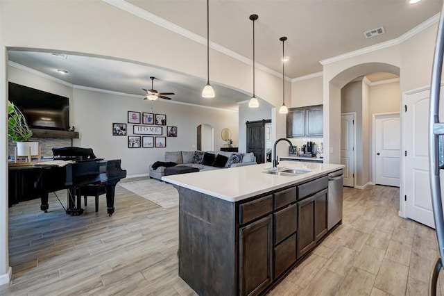 kitchen with arched walkways, a sink, open floor plan, dark brown cabinets, and stainless steel dishwasher