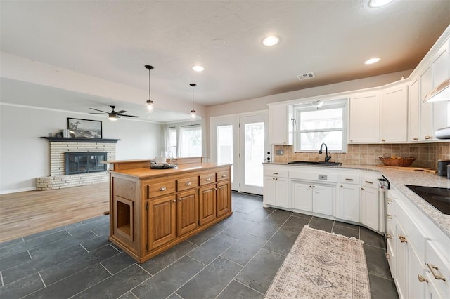 kitchen featuring visible vents, a kitchen island, a fireplace, a sink, and backsplash