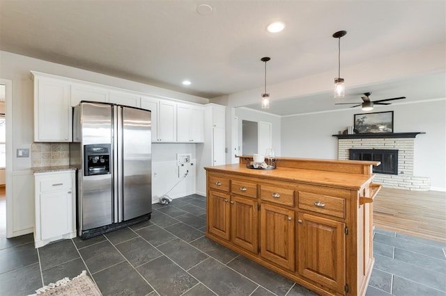 kitchen featuring a fireplace, hanging light fixtures, stainless steel fridge, white cabinets, and tasteful backsplash