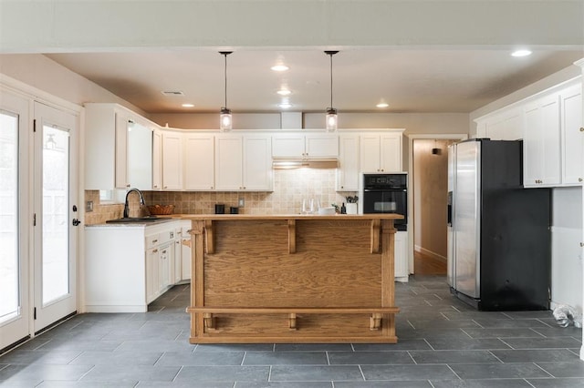 kitchen with backsplash, black oven, stainless steel fridge with ice dispenser, plenty of natural light, and white cabinets