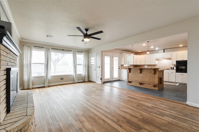 unfurnished living room featuring a wealth of natural light, visible vents, a brick fireplace, and dark wood-style flooring