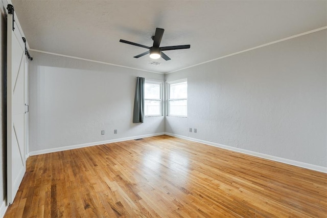 unfurnished room with baseboards, ceiling fan, crown molding, light wood-style floors, and a barn door