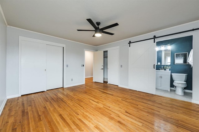 unfurnished bedroom featuring light wood finished floors, two closets, a barn door, and ornamental molding