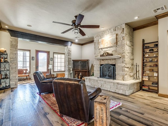 living area featuring visible vents, ceiling fan, wood finished floors, crown molding, and a stone fireplace