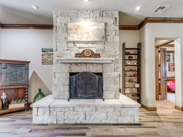 living room featuring baseboards, visible vents, ornamental molding, wood finished floors, and a stone fireplace