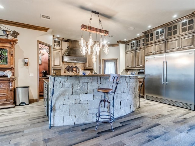 kitchen featuring crown molding, custom range hood, visible vents, backsplash, and built in refrigerator