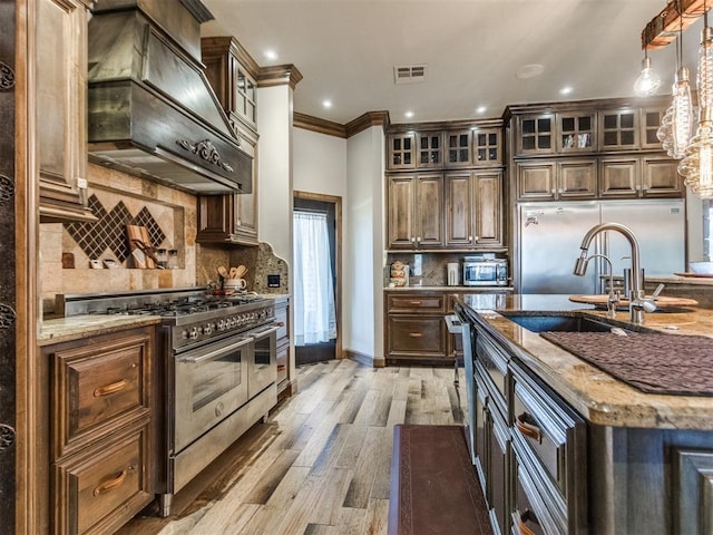 kitchen with light wood finished floors, custom exhaust hood, stainless steel appliances, visible vents, and light stone countertops