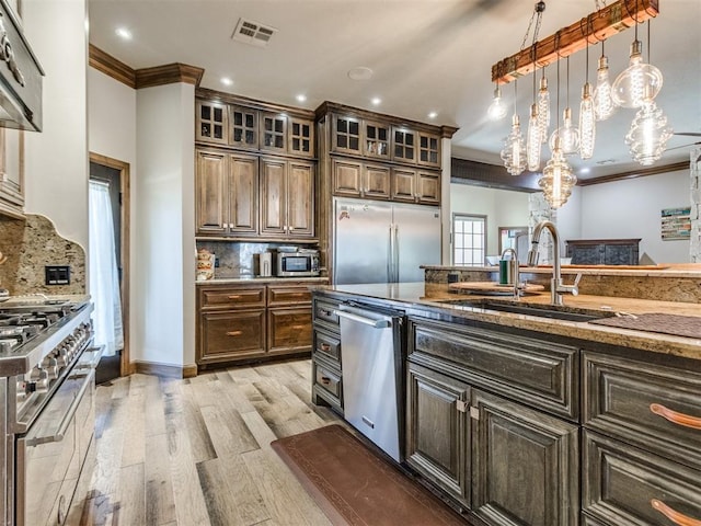 kitchen featuring premium appliances, light wood-style flooring, a sink, visible vents, and ornamental molding