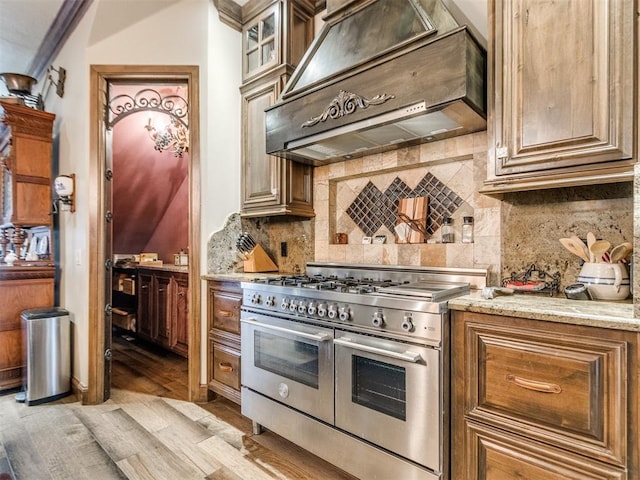 kitchen featuring range with two ovens, decorative backsplash, glass insert cabinets, light stone countertops, and extractor fan