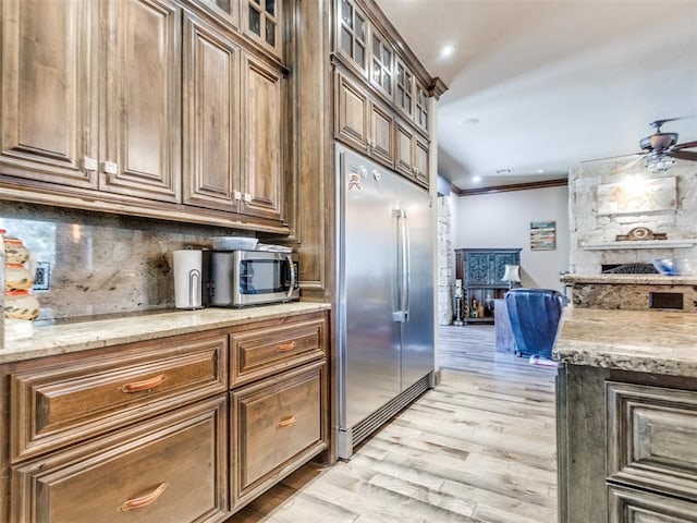 kitchen featuring crown molding, light wood finished floors, tasteful backsplash, appliances with stainless steel finishes, and light stone countertops