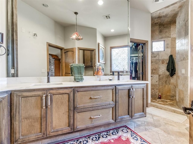 bathroom featuring double vanity, visible vents, a sink, and tiled shower