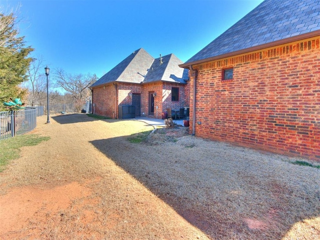 view of home's exterior featuring a high end roof, a patio area, brick siding, and fence