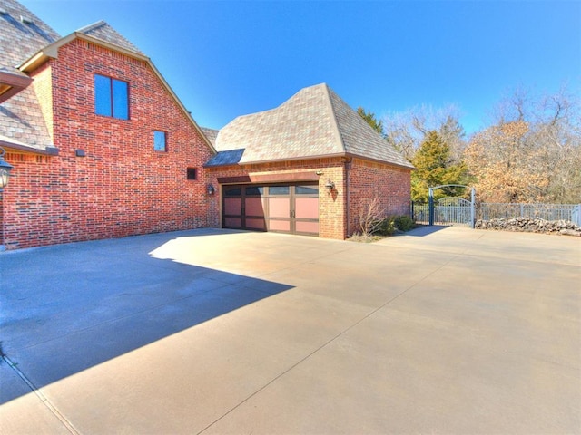 view of side of home with a garage, concrete driveway, brick siding, and fence