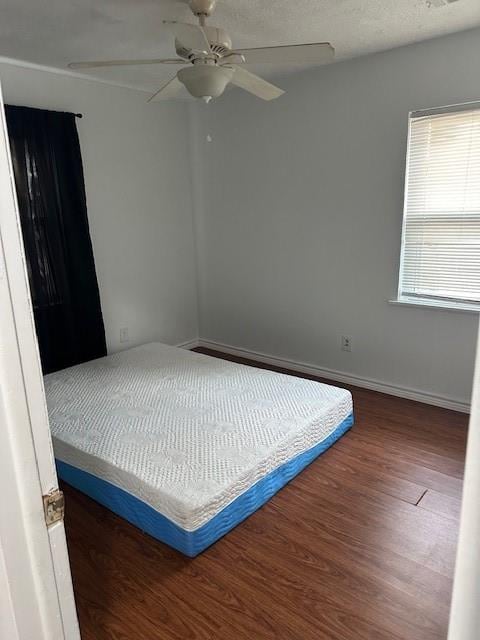 bedroom with a ceiling fan, a textured ceiling, baseboards, and wood finished floors