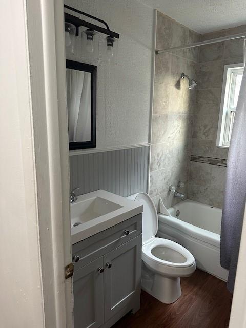 bathroom featuring toilet, a wainscoted wall, wood finished floors, vanity, and bathing tub / shower combination