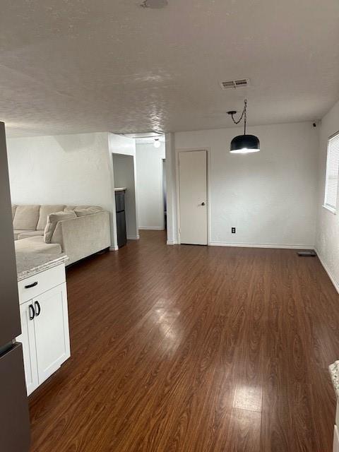 unfurnished living room with dark wood-style floors, baseboards, and visible vents