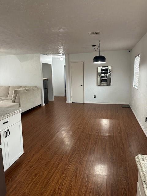 unfurnished living room featuring baseboards, visible vents, and dark wood-type flooring